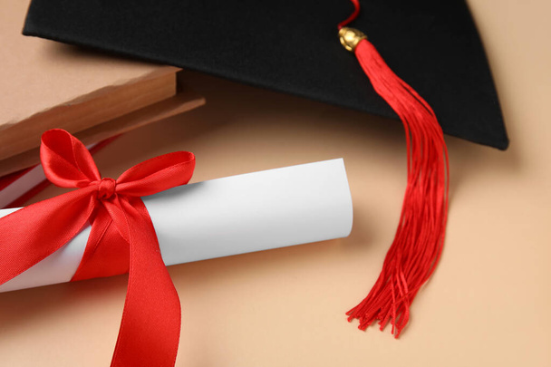 Kırmızı kurdeleli diploma, mezuniyet şapkası ve bej arka plan kitapları. - Fotoğraf, Görsel