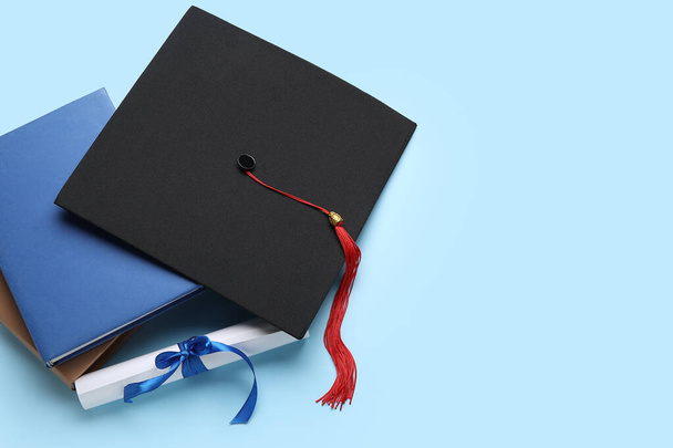 Diploma con cinta, sombrero de graduación y libros sobre fondo azul - Foto, imagen