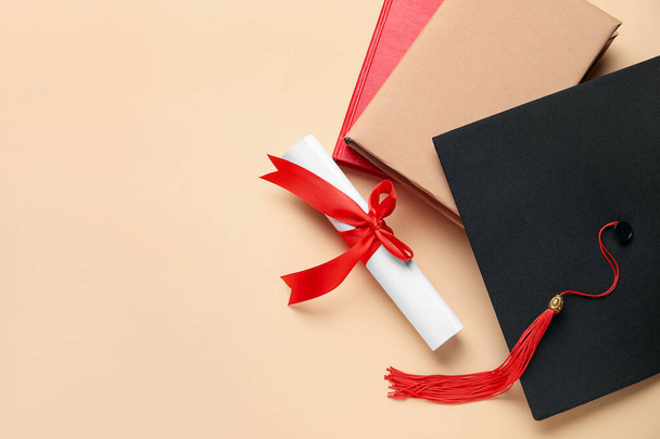 Diploma piros szalaggal, ballagási kalap és könyvek bézs háttér - Fotó, kép