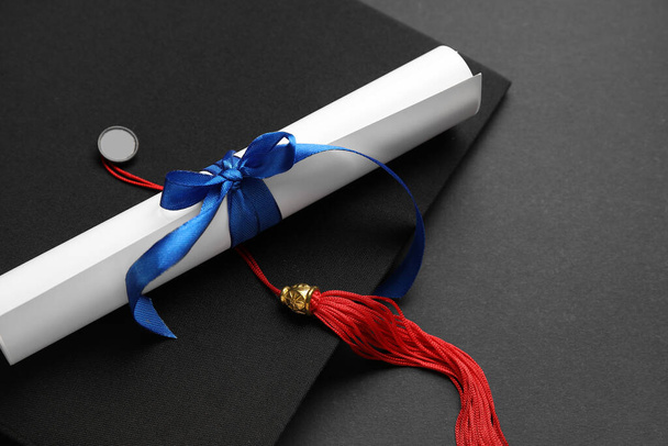 Diplom mit blauer Schleife und Diplomhut auf schwarzem Hintergrund - Foto, Bild