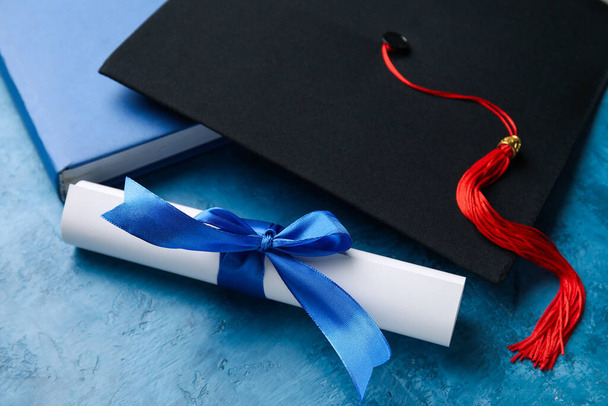 Diplôme avec ruban, chapeau de graduation et livre sur table bleue - Photo, image