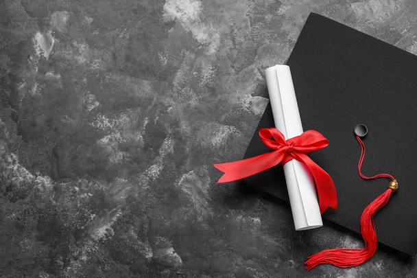 Diploma piros szalaggal és ballagási kalappal a sötétszürke asztalon - Fotó, kép