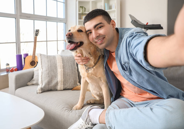 Młody mężczyzna z uroczym psem Labrador robi selfie w domu - Zdjęcie, obraz