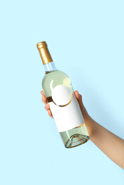 Female hand holding bottle of white wine on blue background - Foto, immagini