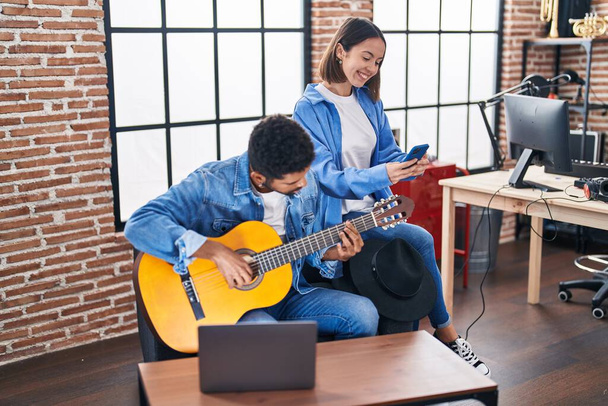 男性と女性のミュージシャンが音楽スタジオでスマートフォンを使ってクラシックギターを演奏 - 写真・画像