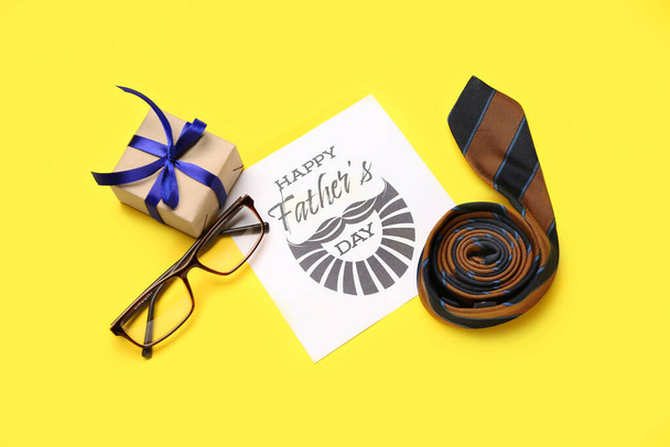 Tarjeta con texto FELIZ DÍA DEL PADRE, corbata de cuello, anteojos y regalo sobre fondo amarillo - Foto, Imagen
