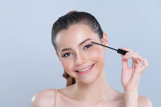 Closeup woman with blond hair putting glamorous black mascara with brush in hand on long thick eyelash. Perfect soft natural cosmetic makeup clean facial skin young woman in isolated background. - Foto, afbeelding