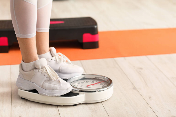 Jeune femme sportive mesurant son poids sur des balances en salle de gym, gros plan - Photo, image