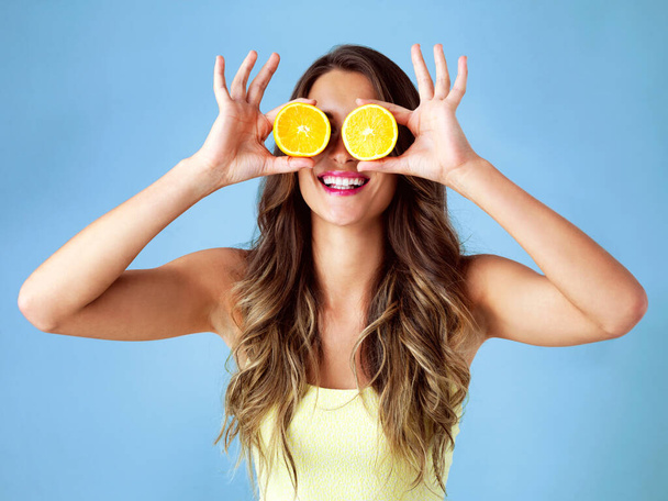 健康的な食べ物は幸せな食べ物です。スタジオショットの若い女性カバー彼女の目にオレンジで青の背景 - 写真・画像