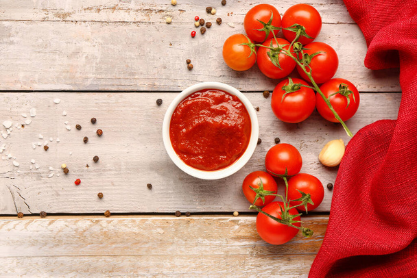 Bowl with tasty tomato paste and fresh vegetables on light wooden background - Foto, Imagen