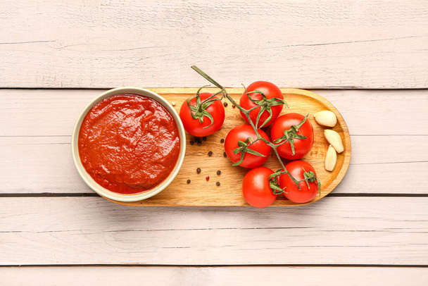 Bowl with tasty tomato paste and fresh vegetables on light wooden background - Фото, изображение