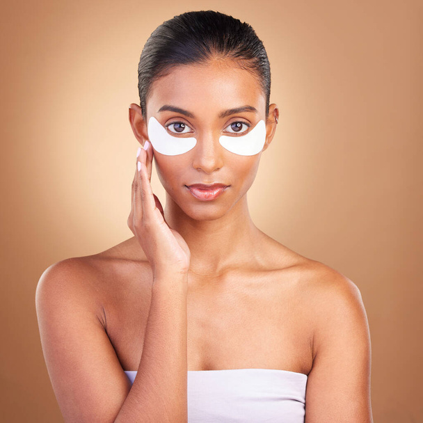 Beauty, eye patch and portrait of Indian woman in studio for facial, spa treatment and glow. Self care, cosmetics and hydration with female model on brown background for mask, product and youth. - Foto, Imagem