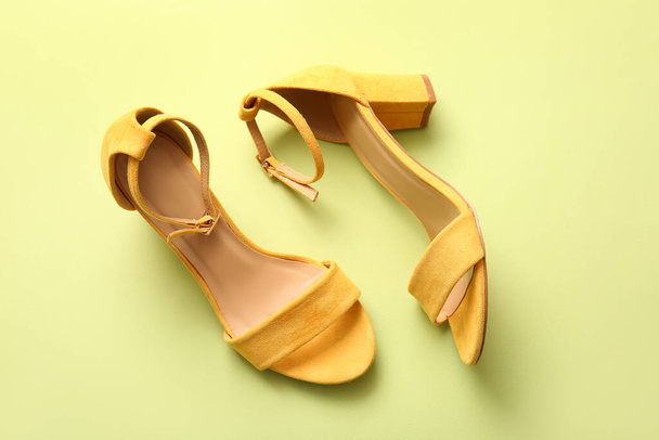 Pair of stylish high heeled sandals on green background - 写真・画像