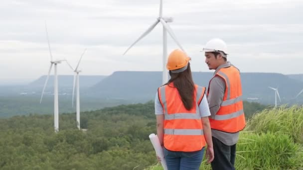 Ingenieros masculinos y femeninos trabajando en un parque eólico en lo alto de una colina o montaña en el campo. Ideales progresivos para la producción futura de energía renovable y sostenible. - Metraje, vídeo