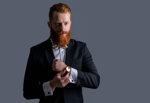 man wearing elegant wrist watch and tuxedo, copy space. tuxedo fashion. handsome bearded man in tuxedo with wrist watch isolated on grey background. man studio shot in tuxedo and wrist watch. - Photo, image
