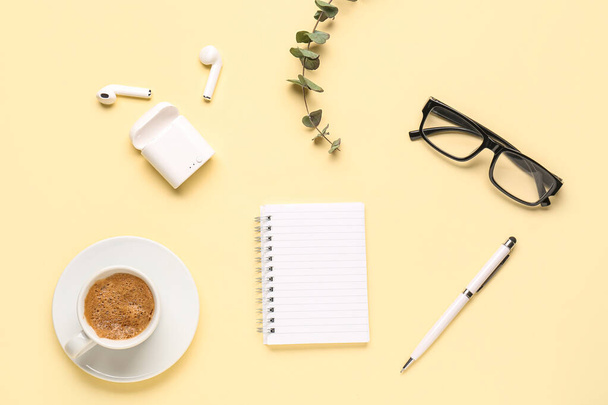 Komposition mit leerem Notizbuch, Kaffeetasse und Gläsern auf gelbem Hintergrund - Foto, Bild