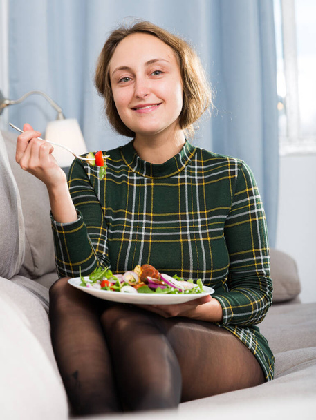 Young woman sitting on sofa at home and eating healthy food - Foto, Imagem