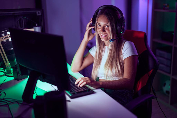 Young beautiful hispanic woman streamer playing video game using computer at gaming room - Foto, afbeelding