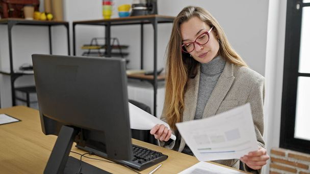 Mujer joven caucásica trabajadora de negocios utilizando el documento de lectura de computadoras en la oficina - Foto, imagen