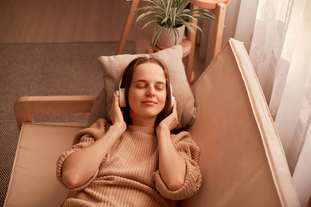 Porträt einer fröhlich entspannten kaukasischen jungen Frau, die Musik hört, während sie sich zu Hause auf der Couch ausruht, die Augen geschlossen hält, ruhig und glücklich ist und ihr Lieblingslied genießt. - Foto, Bild