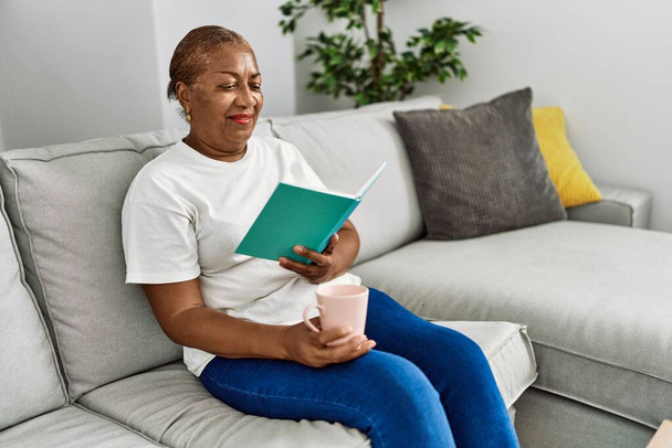 Mujer afroamericana mayor bebiendo libro de lectura de café en casa - Foto, imagen