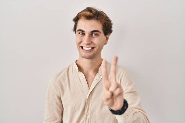 Young man standing over isolated background showing and pointing up with fingers number two while smiling confident and happy.  - Photo, Image
