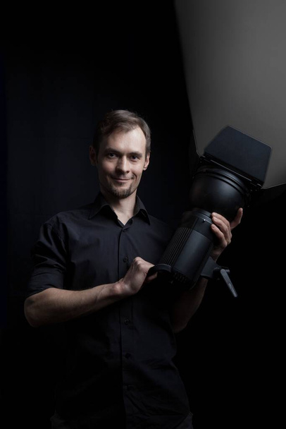 Portret gaffera z profesjonalnym urządzeniem oświetleniowym w dłoniach na czarnym tle. - Zdjęcie, obraz
