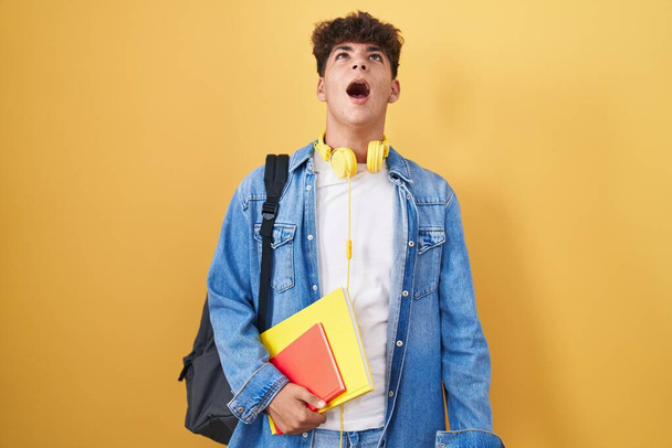 Hispanic teenager wearing student backpack and holding books angry and mad screaming frustrated and furious, shouting with anger. rage and aggressive concept.  - Foto, Bild