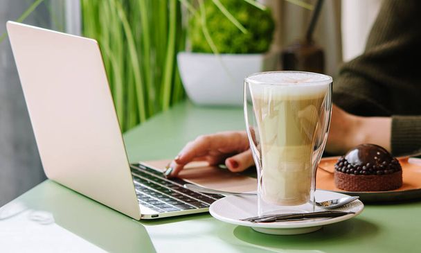 Junge Frau benutzt Laptop mit Dessert und Tasse Kaffee im Café - Foto, Bild