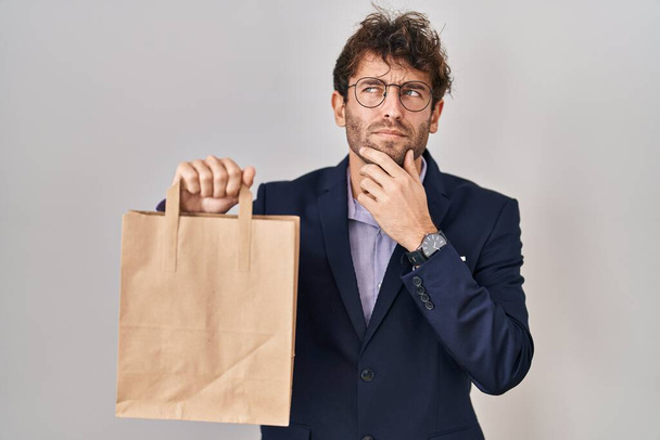 Spanyol üzletember tartja szállítási táska komoly arc gondolkodás kérdés kézzel az állon, gondolkodó zavaros ötlet  - Fotó, kép