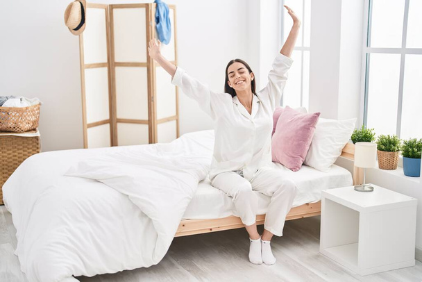 Young hispanic woman waking up sitting on bed at bedroom - Photo, Image
