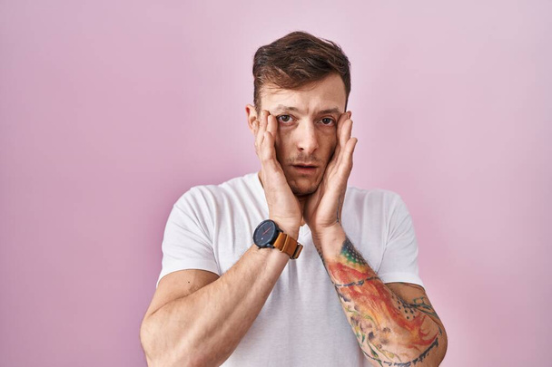 Caucasian man standing over pink background tired hands covering face, depression and sadness, upset and irritated for problem  - Photo, Image