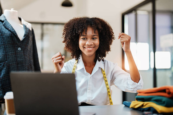 feliz sorriso jovem adolescente afro-americano designer de moda elegante usando laptop computador trabalhando no estúdio de negócios de moda de sucesso. - Foto, Imagem