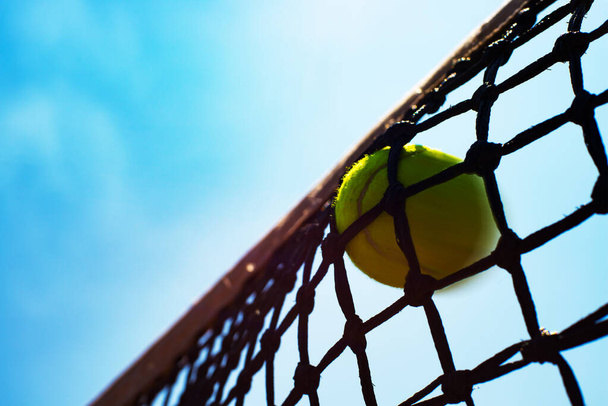 Yellow tennis ball hits in the net during game. Blue sky at background - Photo, Image