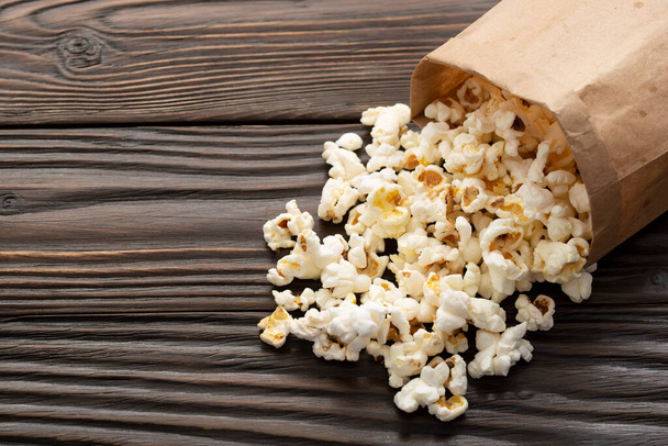 Popped corn snack in paper bag on wooden table closeup - Foto, afbeelding