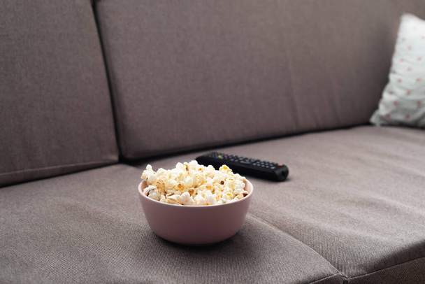 Bowl with popcorn and tv remote control on sofa  - Fotó, kép