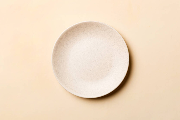 Вид сверху на изолированный цветной фон пустой круглой бежевой тарелки для еды. Пустое блюдо с местом для дизайна. - Фото, изображение