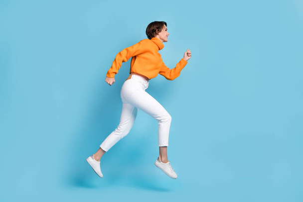 Full size photo of pretty young girl profile view running hurry speed fast dressed stylish orange look isolated on blue color background. - Φωτογραφία, εικόνα