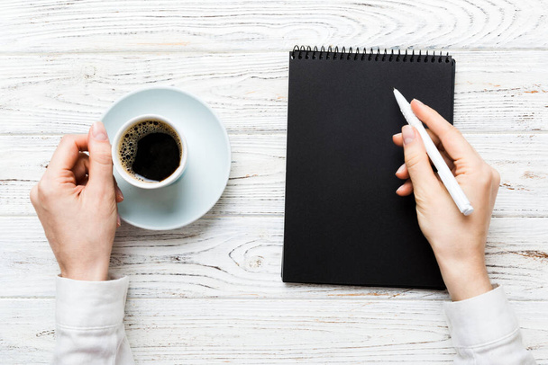 Kobieta ręka z ołówkiem na notatniku i trzymać filiżankę kawy. Kobieta pracująca na stole biurowym z kawą. - Zdjęcie, obraz