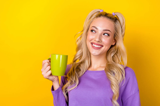Фото мечтательной блестящей леди, одетой в фиолетовую рубашку и пьющей горячий чай, выглядящий пустым изолированным желтым цветом фона. - Фото, изображение