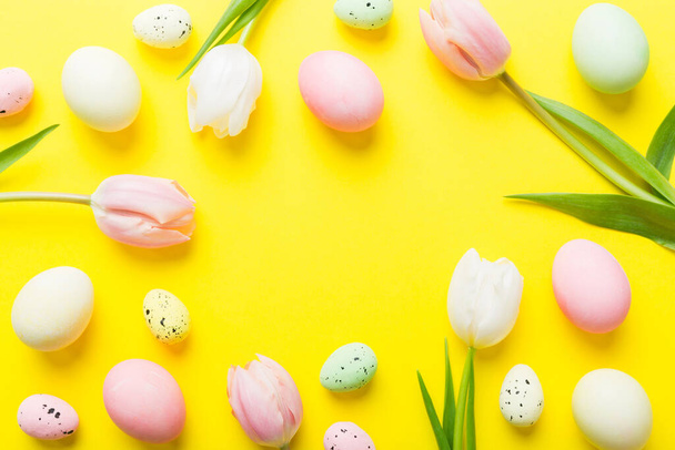 Feliz composição pascal. Ovos de Páscoa na mesa colorida com tulipas amarelas. Ovos coloridos tingidos naturais vista superior de fundo com espaço de cópia. - Foto, Imagem