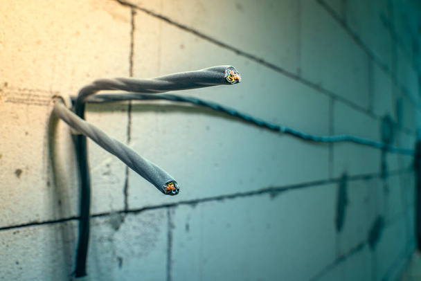 Close-up of two three-wire wires attached to the wall. Wiring of electrical wiring on the wall of aerated concrete bricks. Power electrical wires in black braid for sockets - Fotoğraf, Görsel