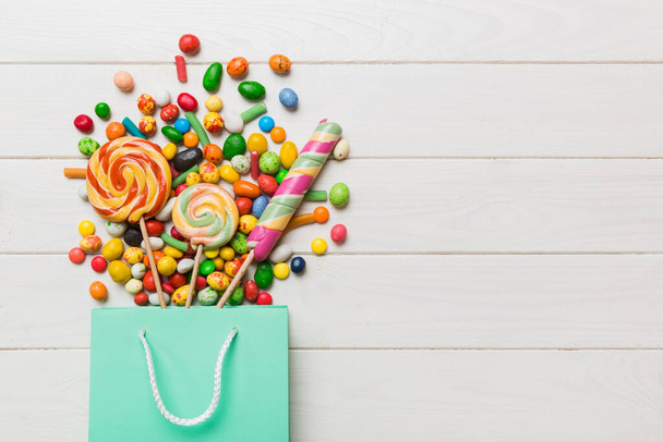 shopping paper gift bag in corner full of assorted traditional candies falling out on colored background with copy space. Happy Holidays sale concept. - Foto, Imagem