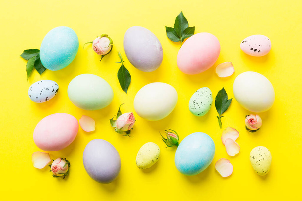 Feliz Pascua. Huevos de Pascua sobre mesa de colores con rosas amarillas. Huevos coloridos teñidos naturales vista superior de fondo con espacio de copia. - Foto, imagen