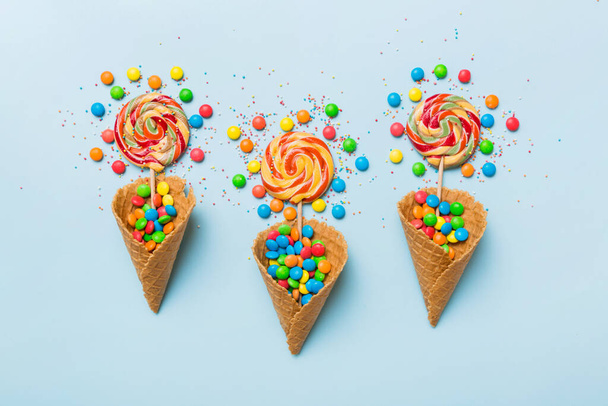 waffle cone full of assorted traditional candies falling out on colored background with copy space. Happy Holidays sale concept. - Photo, image