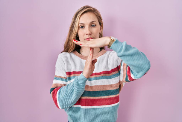 Young blonde woman standing over pink background doing time out gesture with hands, frustrated and serious face  - Photo, image