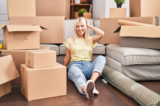 Young blonde woman smiling confident relaxed sitting on floor at new home - Foto, imagen