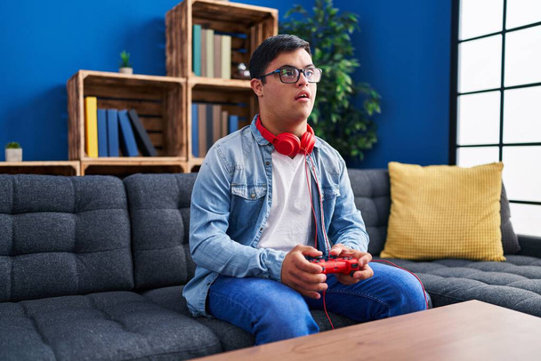Человек с синдромом Дауна играет в видеоигры, сидя дома на диване - Фото, изображение