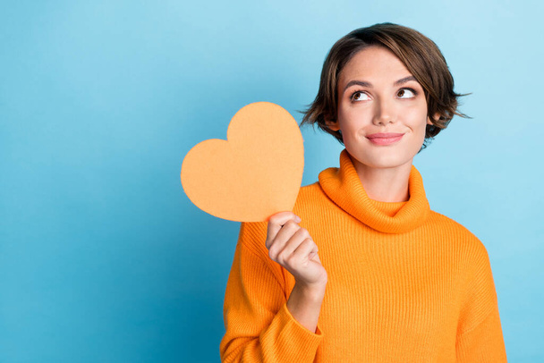 Photo portrait of lovely young lady hold paper heart look empty space dressed stylish orange clothes isolated on blue color background. - 写真・画像