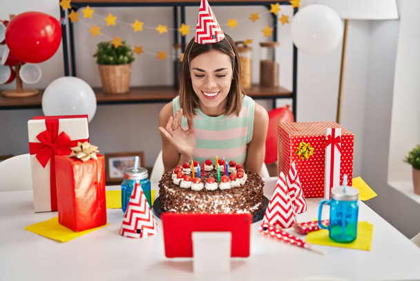 Молодая красивая латиноамериканка празднует онлайн день рождения сидя дома на столе - Фото, изображение